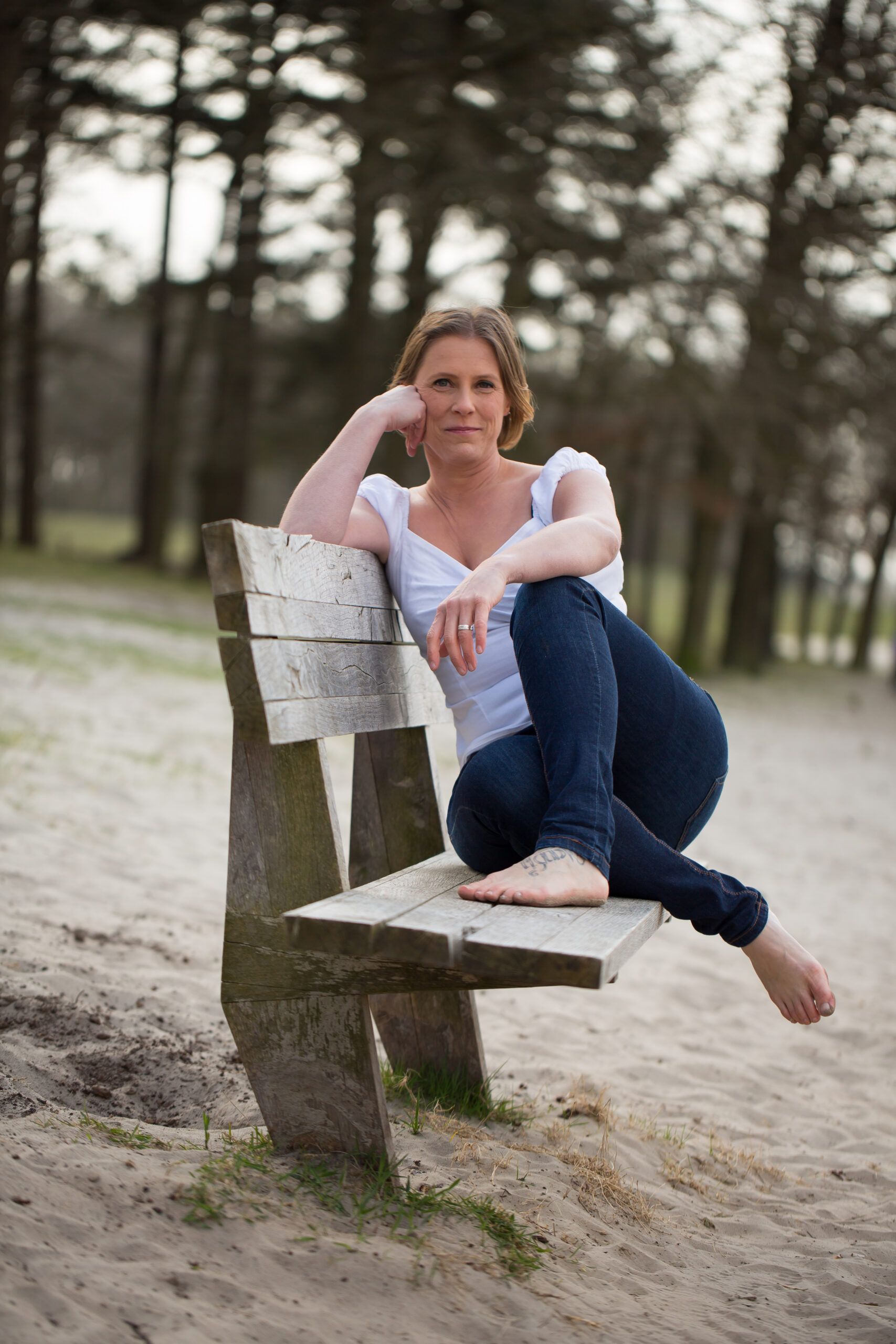 Op de foto zie je Claudia Stinne die in de camera kijkt. Ze zit relaxt op een bankje en steunt daar met haar ellebogen op.