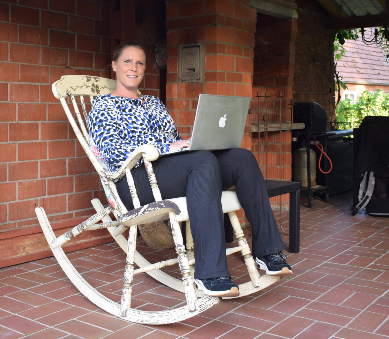 Claudia Stinne - schrijfcoach - zit op de veranda in een schommelstoel met haar laptop