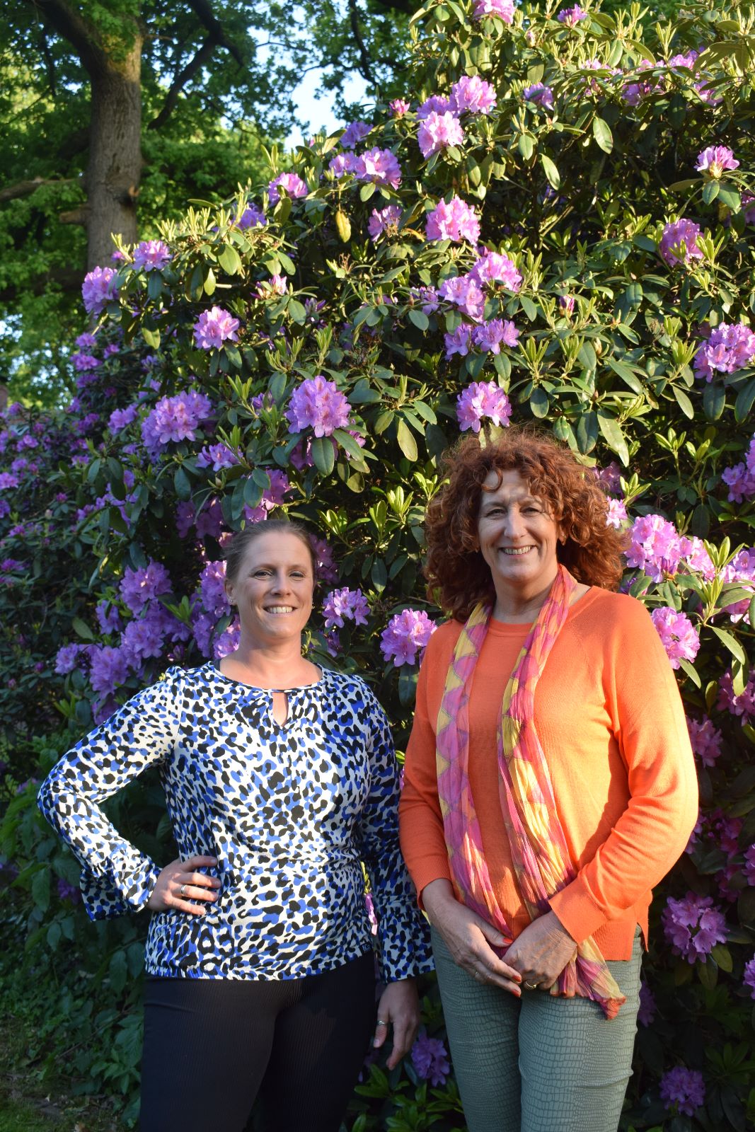 Claudia Stinne en Lieza Geuzinge voor een bloeiende Rodondendronstruik met paarse bloemen